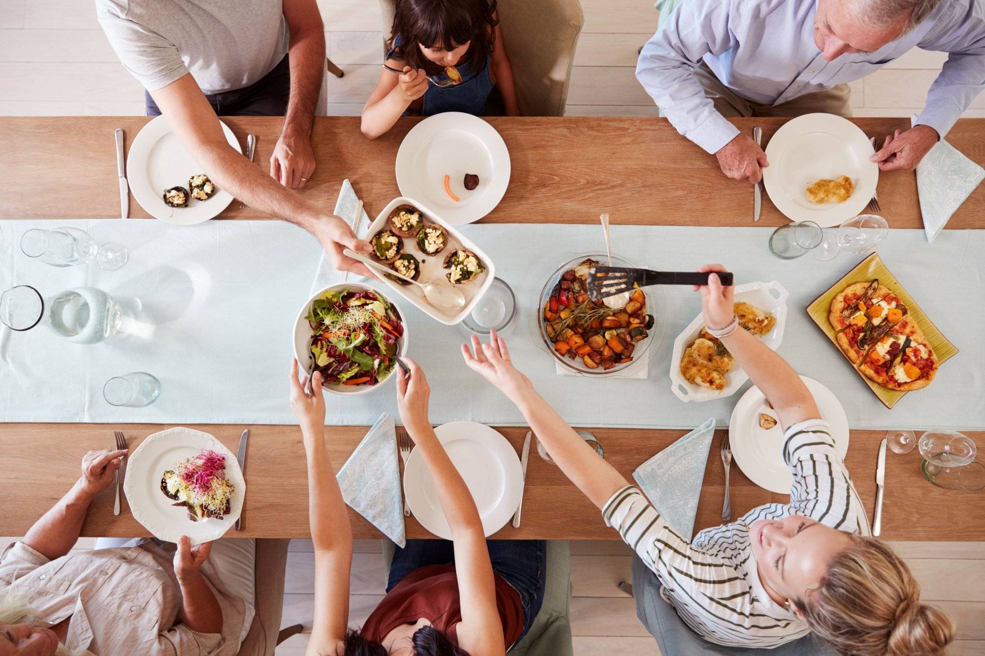 Three generation white family sitting at a dinner table together serving a meal, overhead view Three generation white family sitting at a dinner table together serving a meal, overhead view