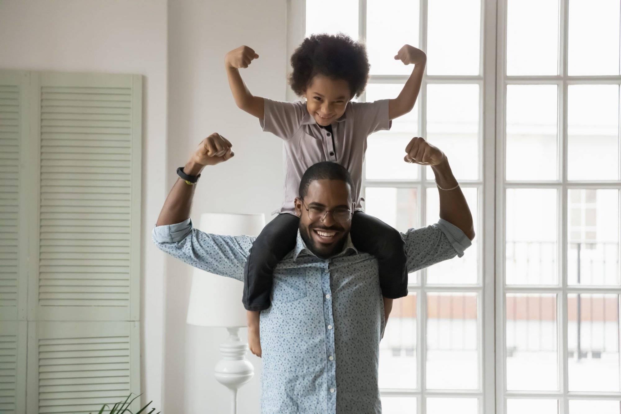 African ethnicity little son sitting on fathers shoulders showing biceps African ethnicity little son sitting on fathers shoulders showing biceps